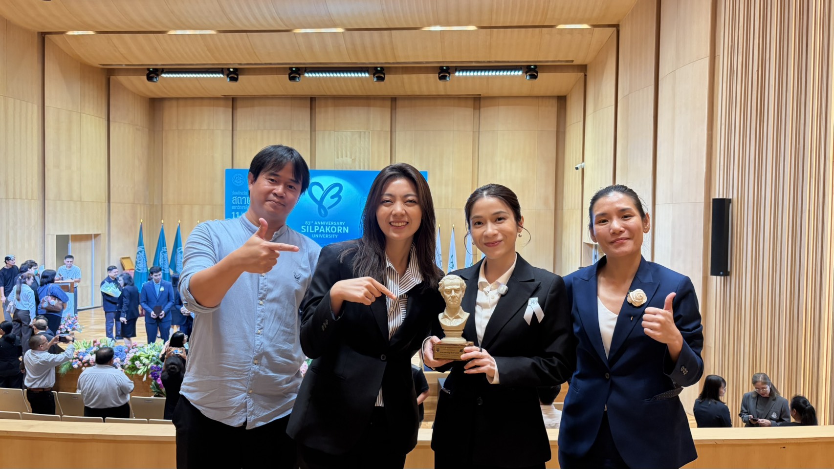 แหวน เยาวณัฐ ถือรางวัลพร้อมผู้ร่วมงานสามคนในหอประชุมมหาวิทยาลัยศิลปากร